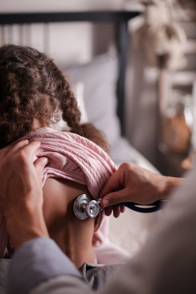 Doctor using stethoscope to check childs back during a health examination indoors.